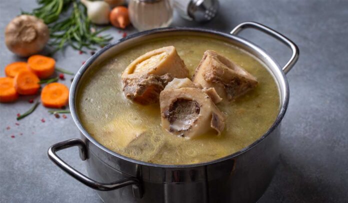 Panela de inox sobre uma mesa com caldo de ossos