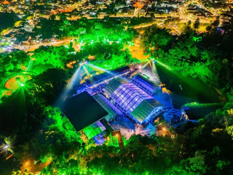 Vista aérea do Warung Day Festival 2026, realizado na Pedreira Paulo Leminski e na Ópera de Arame, em Curitiba, com público e estrutura iluminada.