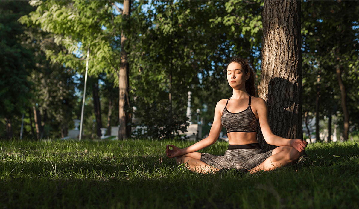 Mulher praticando yoga ao ar livre em um parque, sentada em posição de meditação, simbolizando detox pós-festas, equilíbrio corporal e bem-estar em uma rotina sem glúten.