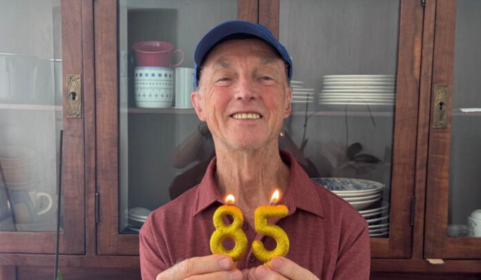 Meu pai Vilson Kupczik aos 85 anos segurando velas de aniversário douradas em forma de número 85 na cozinha