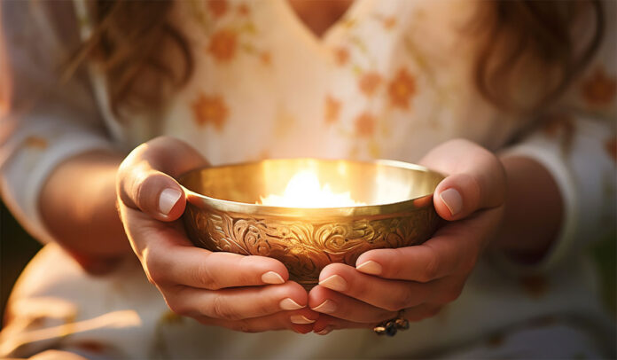 Mãos segurando tigela tibetana dourada com luz suave durante prática meditativa - 4ºEncontro Holístico Universo