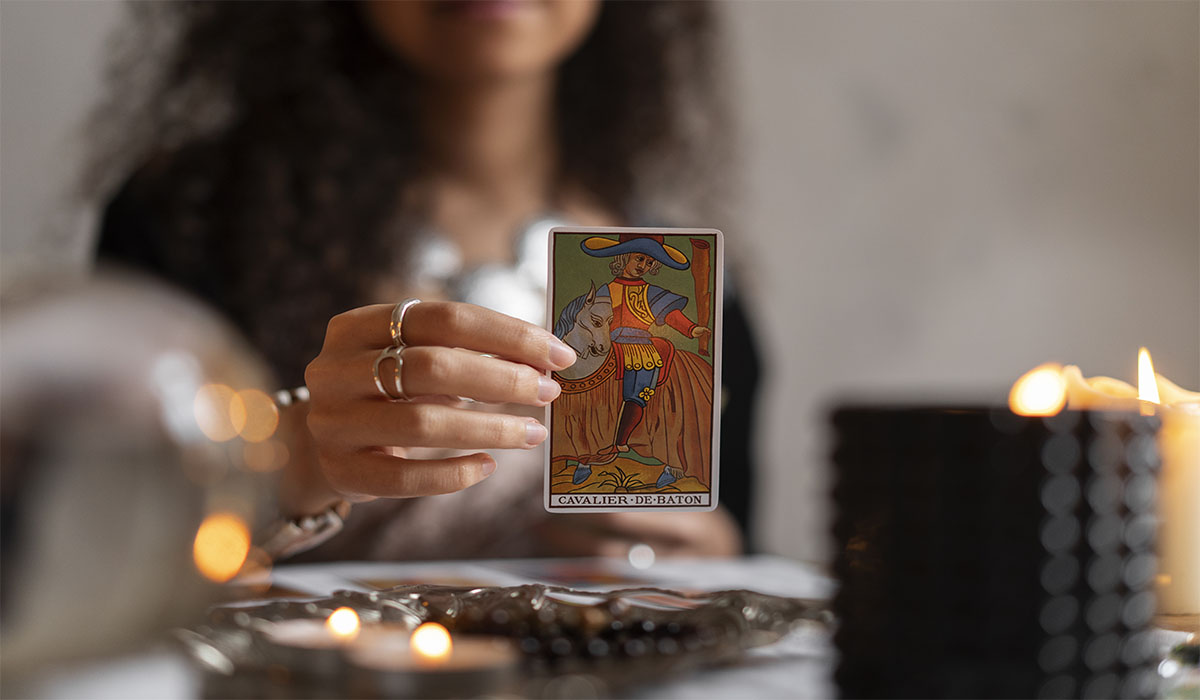 Oraculista segurando carta de tarot Cavalier de Baton em sessão com velas acesas ao fundo